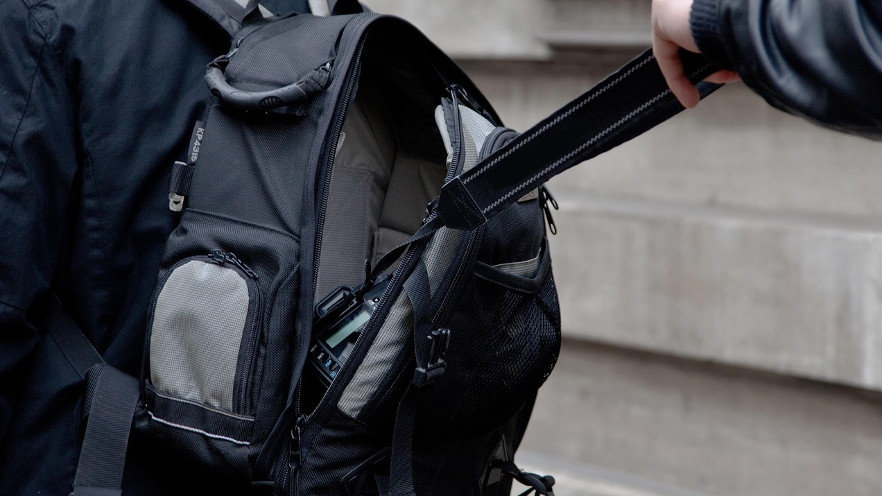 Una persona robant una càmera d'una motxilla pel carrer.
